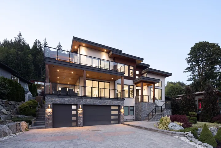 Contemporary house with a balcony, stairs, stone siding, an attached garage, and decorative driveway