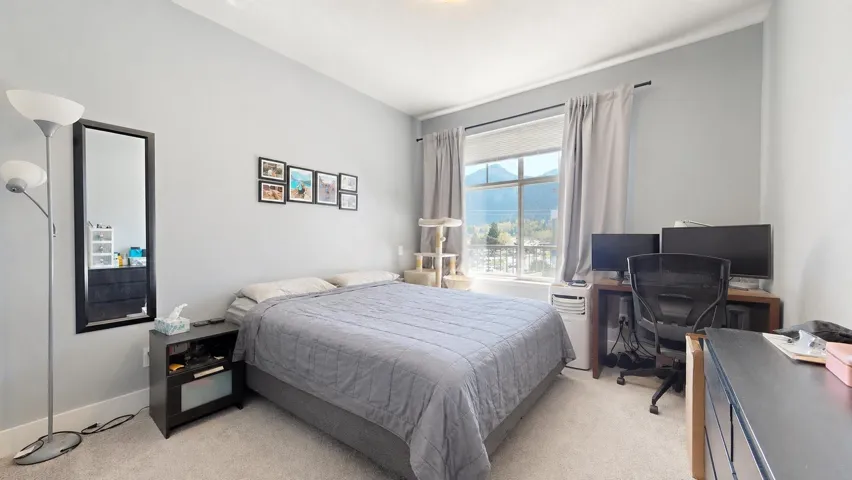 Bright bedroom featuring light gray walls, plush carpeting, a large window offering mountain scenery, and white trim molding