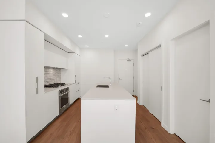 Modern kitchen featuring an integrated island, stainless steel gas range and oven, hexagon tile backsplash, recessed lighting, and wood-finish flooring