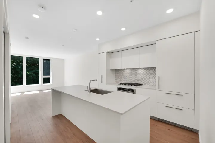 Modern kitchen featuring a white island with an undermount sink and stainless steel faucet, flat-panel cabinetry, a gas cooktop, and a white hexagonal tile backsplash