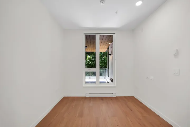 Spacious room featuring wood-finish flooring, white walls, and a large window