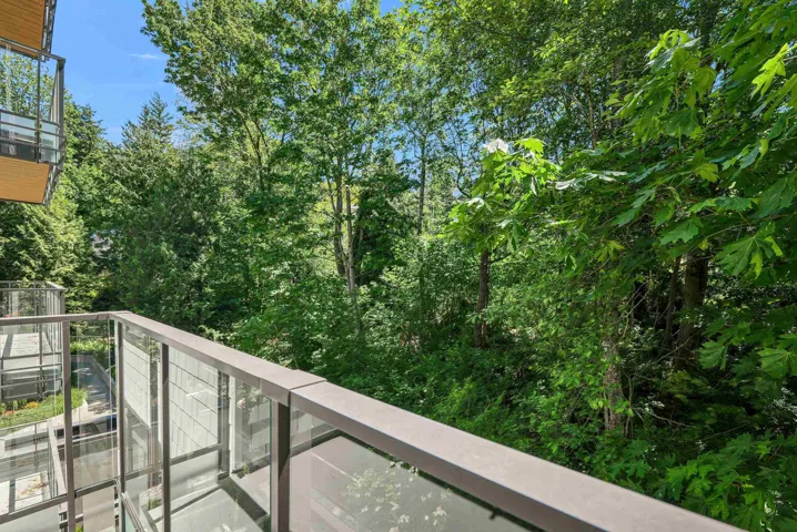 Balcony featuring glass and metal railings, overlooking a dense canopy of mature trees