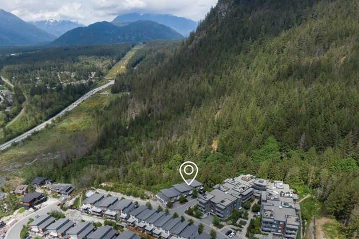 Aerial view of property and surrounding area featuring a forest, a mountainous background, and nearby suburban area