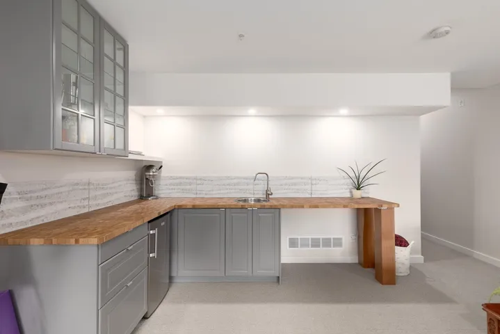 Kitchen with gray cabinets, wooden counters, a sink, and glass insert cabinets
