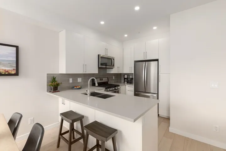 Kitchen with stainless steel appliances, a peninsula, a kitchen bar, light wood-type flooring, and recessed lighting