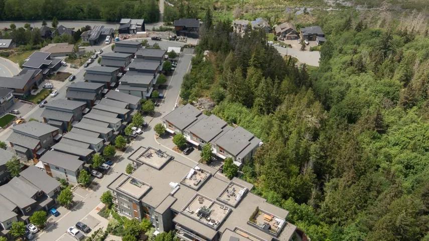 Aerial view of property and surrounding area featuring nearby suburban area and a heavily wooded area