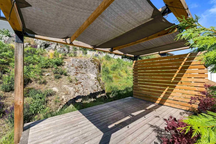 Outdoor deck with wood-finish flooring, a slatted privacy wall, and a pergola featuring shade fabric