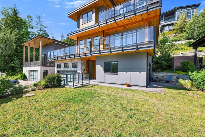 Modern multi-level exterior featuring extensive glass railings, wood soffits, stone accents, multiple balconies, and a two-car garage
