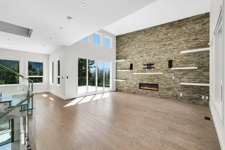 Spacious living area featuring a stacked stone accent wall with an inset linear fireplace, wood-finish flooring, and multiple large windows