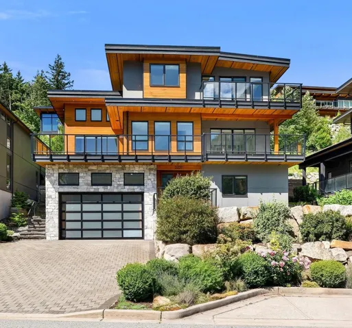 Modern architectural residence featuring multiple balconies with glass railings, wood-finish siding, and a stone facade