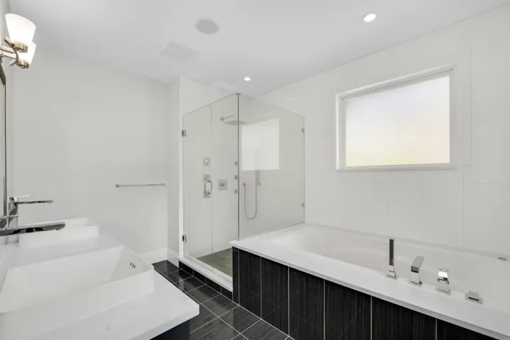 Contemporary bathroom featuring a glass-enclosed shower with multiple sprayers, a rectangular soaking tub with polished chrome fixtures, and a dual-sink vanity with under-mount sinks and polished chrome faucets