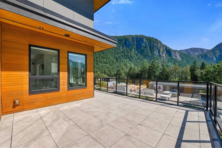 Spacious exterior deck featuring large format tile flooring, a glass railing, and a wood-paneled exterior