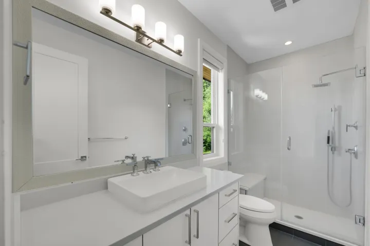 Bathroom featuring a single vanity with vessel sink, wall-mounted mirror, frameless glass shower enclosure, and a built-in shower bench