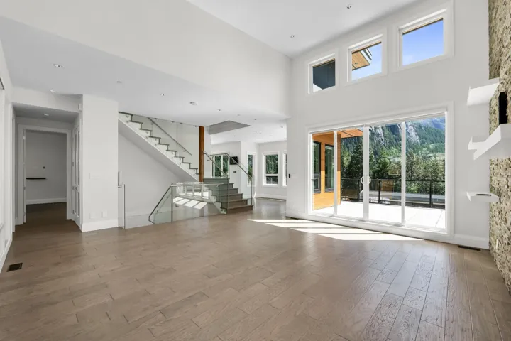 Spacious interior featuring high ceilings, light wood-finish flooring, a contemporary staircase with glass railing, and large sliding glass doors opening to an outdoor patio