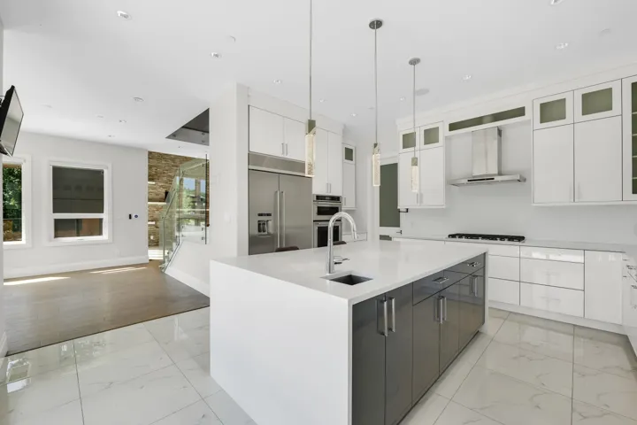 Gourmet kitchen featuring a large central island with integrated sink, stainless steel appliances, white cabinetry, and a gas range with a stainless steel hood