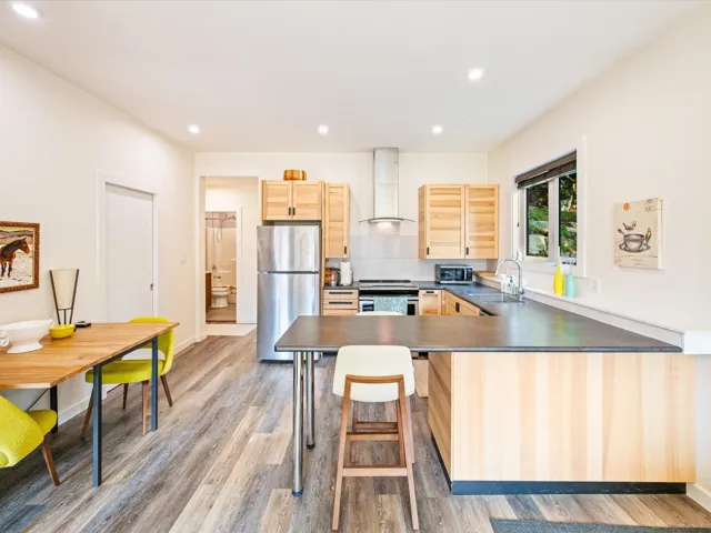 Kitchen featuring light brown cabinetry, dark countertops, stainless steel appliances, a peninsula, and light wood-style flooring