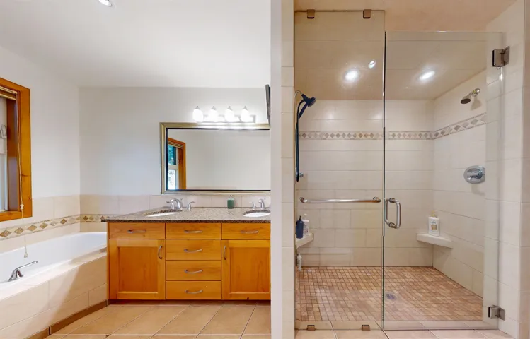 Spacious bathroom featuring a dual vanity with a granite countertop, a soaking tub, and a glass-enclosed shower with multiple showerheads