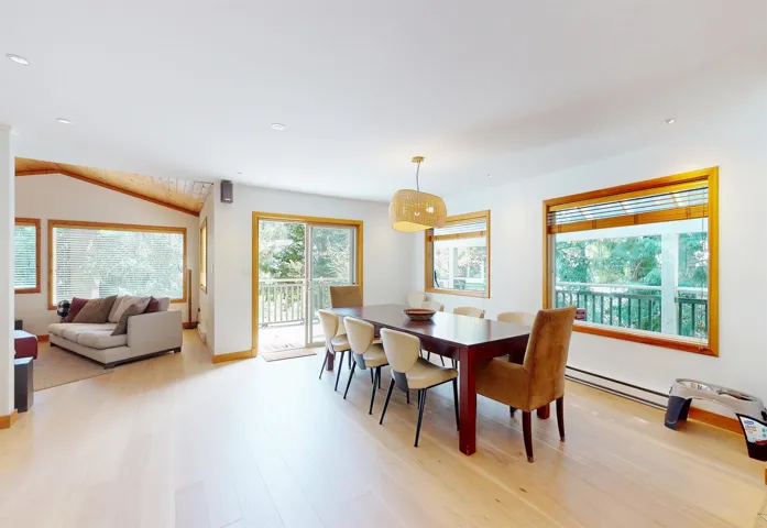 Dining area featuring light wood-finish flooring, a contemporary pendant light fixture, and multiple windows with wood trim