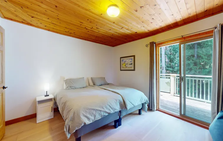 Room featuring a wood-panel ceiling, light wood-finish flooring, and a sliding glass door leading to an outdoor deck