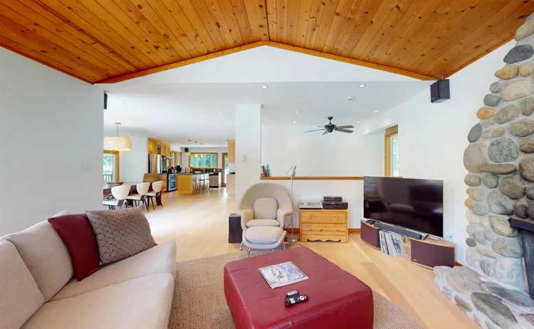 Living area featuring a stone fireplace, wood-finish flooring, a wood-paneled vaulted ceiling, recessed lighting, and an integrated ceiling fan