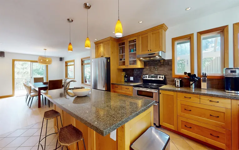 Kitchen featuring a large central island with a vessel sink, stainless steel appliances, wood cabinetry, and granite countertops