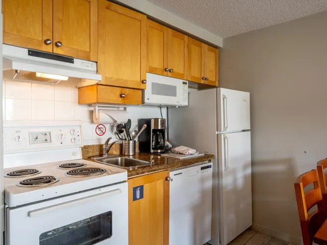 Kitchen with white appliances, under cabinet range hood, tasteful backsplash, a textured ceiling, and brown cabinets