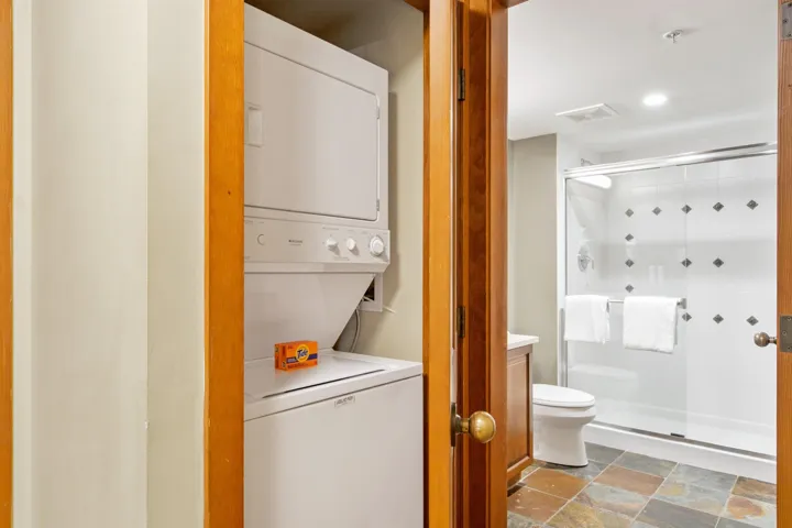 Washroom with stone tile floors and estacked washer and dryer
