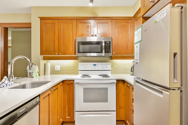 Kitchen featuring stainless steel appliances, brown cabinetry, light stone counters, and tasteful backsplash