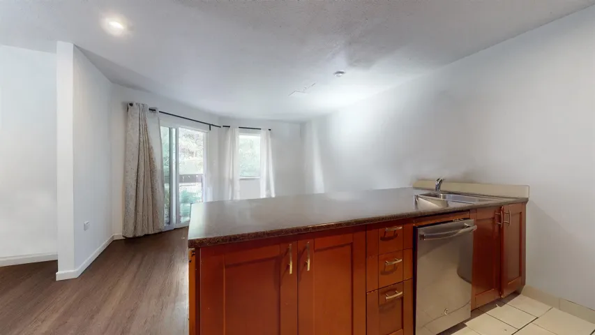 Kitchen with dishwasher, a peninsula, brown cabinets, dark countertops, and light wood-style floors