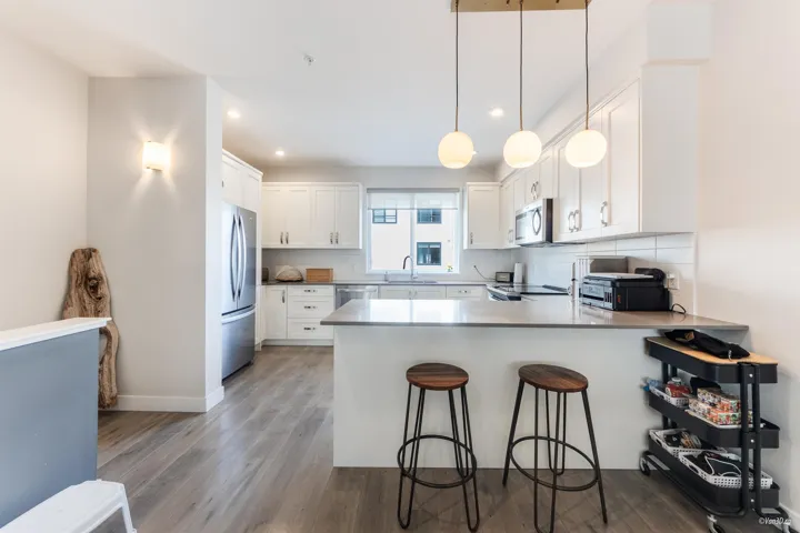 Kitchen featuring a peninsula, decorative backsplash, a breakfast bar, light wood finished floors, and white cabinetry