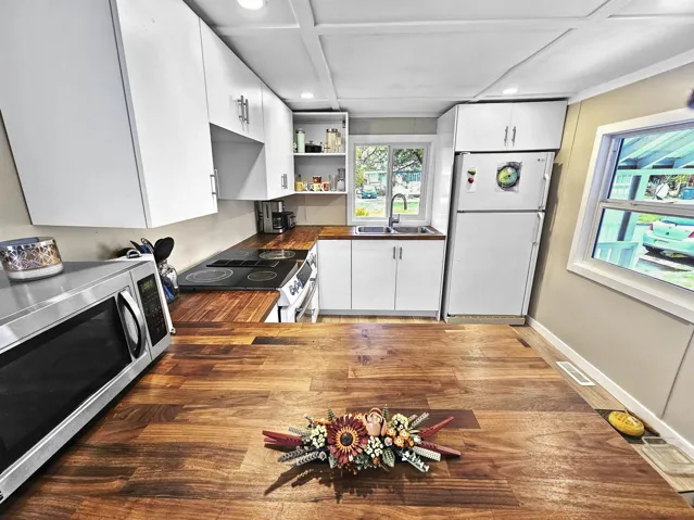 Kitchen featuring stainless steel microwave, freestanding refrigerator, open shelves, a sink, and range with electric stovetop