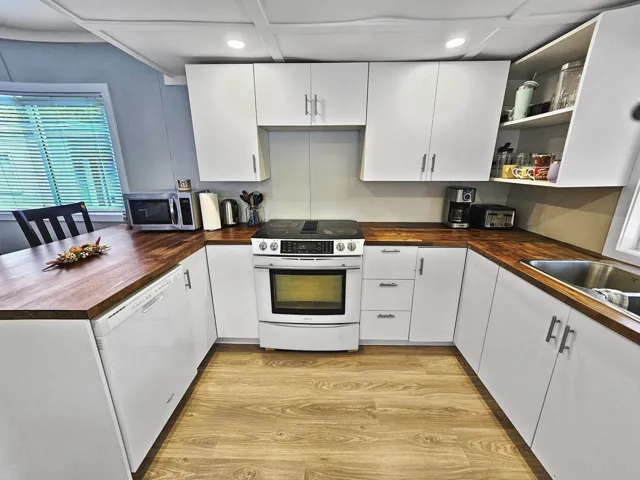 Kitchen with dishwasher, electric stove, butcher block counters, stainless steel microwave, and open shelves