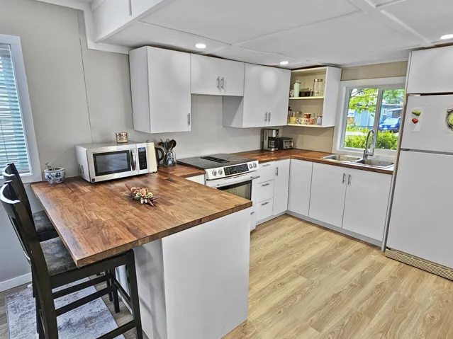 Kitchen featuring a peninsula, a sink, wooden counters, appliances with stainless steel finishes, and light wood finished floors