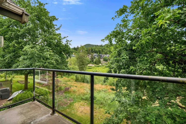 Private balcony with glass panel railing and concrete flooring overlooking natural landscaping and distant mountains