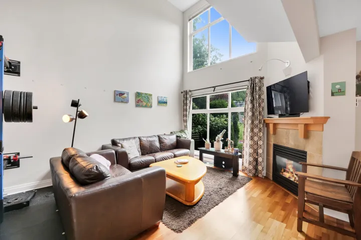 Living area featuring vaulted ceilings, a large accent window, a built-in fireplace with a tile surround and wood mantel, and wood-finish flooring