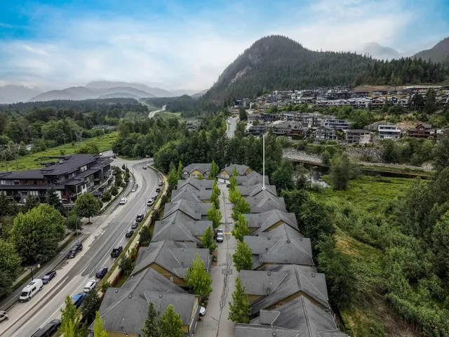 Residential community with uniform rooflines and a central green space, bordered by a roadway and natural landscape