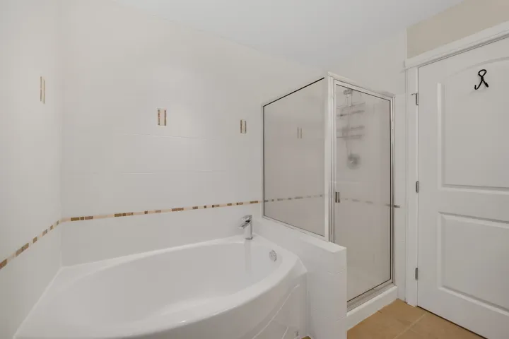 Corner soaking tub with deck-mounted faucet and surrounding white tile