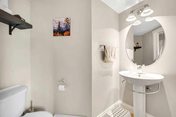Pedestal sink with a chrome faucet, oval mirror, and wall-mounted vanity lighting
