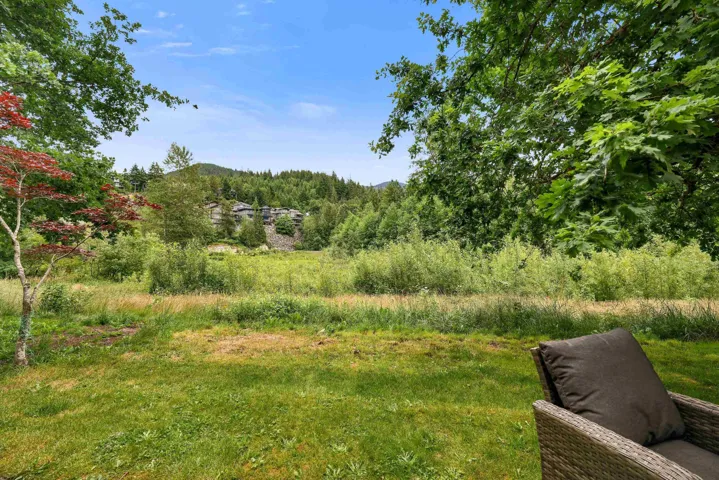 Expansive grassy outdoor space framed by mature trees, featuring distant forested hills and a clear sky