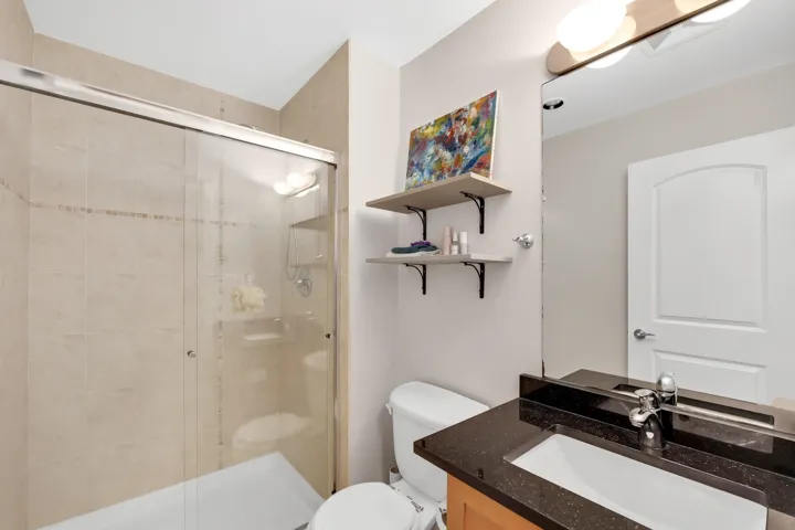 Bathroom featuring a glass-enclosed shower with tile surround, a built-in vanity with a dark countertop and undermount sink, a wall-mounted mirror, and overhead lighting