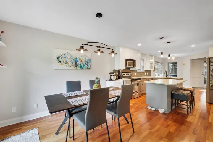 Open-concept living space featuring wood-finish flooring, a modern linear chandelier, and a kitchen with white cabinetry, stainless steel appliances, and a central island with countertop seating