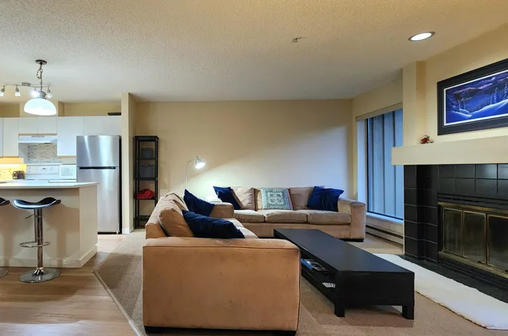 Living area featuring a textured ceiling, light wood-style floors, a fireplace, a baseboard heating unit, and recessed lighting