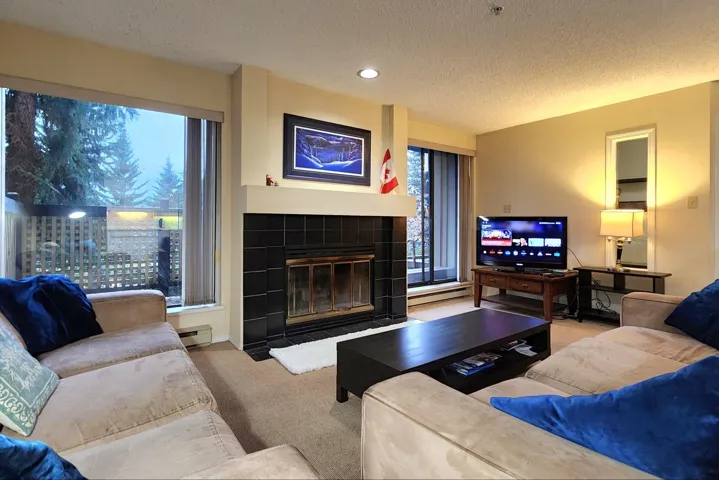 Carpeted living area with a textured ceiling, a tiled fireplace, a baseboard heating unit, and recessed lighting