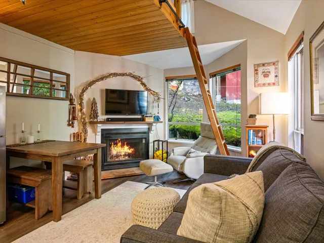 Living room featuring wood finished floors, a warm lit fireplace, vaulted ceiling, and wooden ceiling