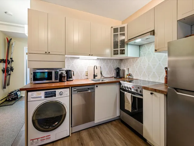 Kitchen featuring washer / clothes dryer, appliances with stainless steel finishes, under cabinet range hood, glass insert cabinets, and backsplash