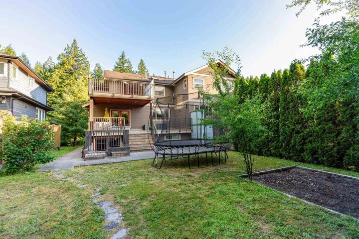 Rear view of property featuring a trampoline, a yard, a patio, a deck, and a balcony