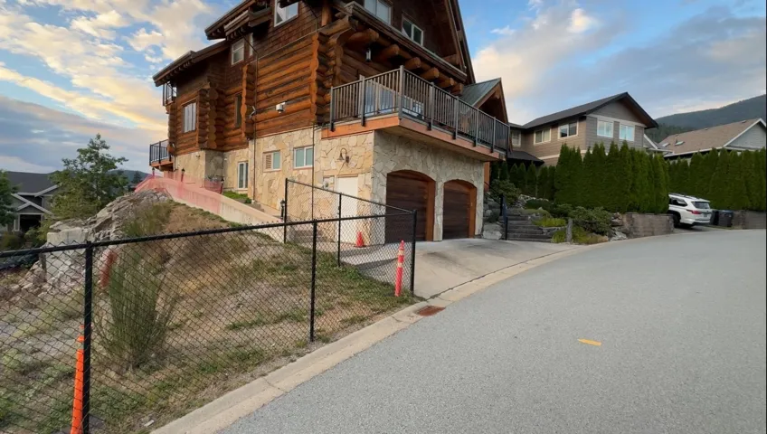 View of front of house featuring stone siding, a balcony, log siding, a garage, and driveway