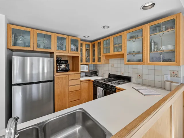 Kitchen featuring light countertops, black / electric stove, freestanding refrigerator, decorative backsplash, and glass insert cabinets
