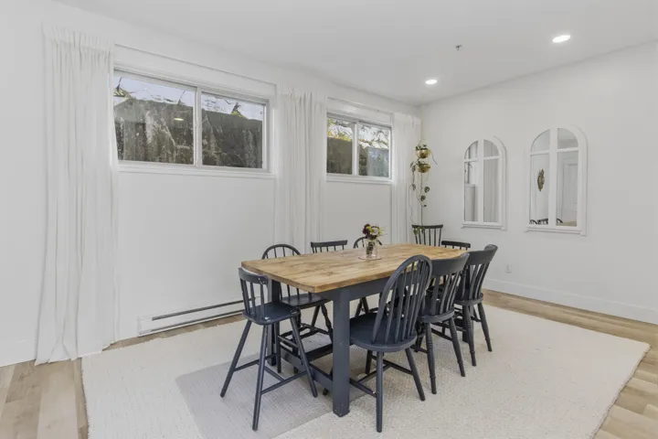 Kitchen featuring stainless steel appliances, wood-finish flooring, white cabinetry, a wood-finish range hood, and a kitchen island with seating
