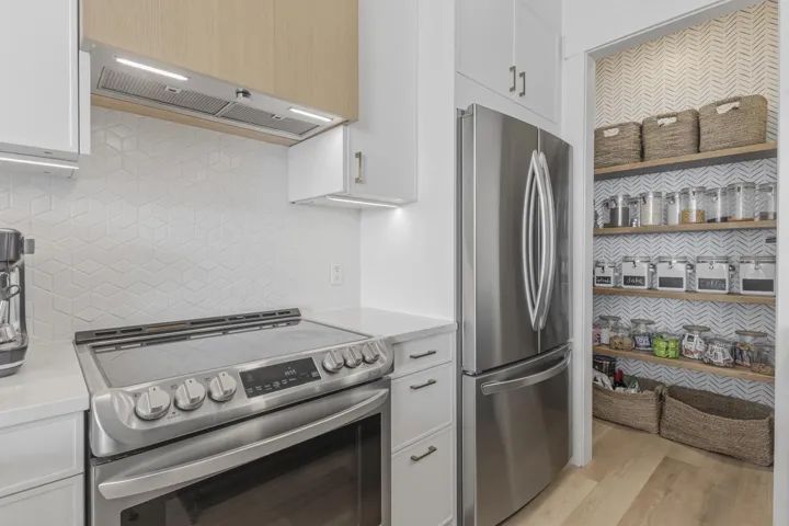 Stainless steel appliances, white cabinetry with silver-tone hardware, geometric pattern backsplash, wood-finish flooring, and a walk-in pantry with wood shelving